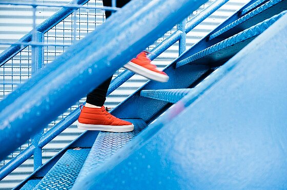 Nahaufnahme von Füßen in roten Schuhen, die eine blaue Treppe hinaufgehen