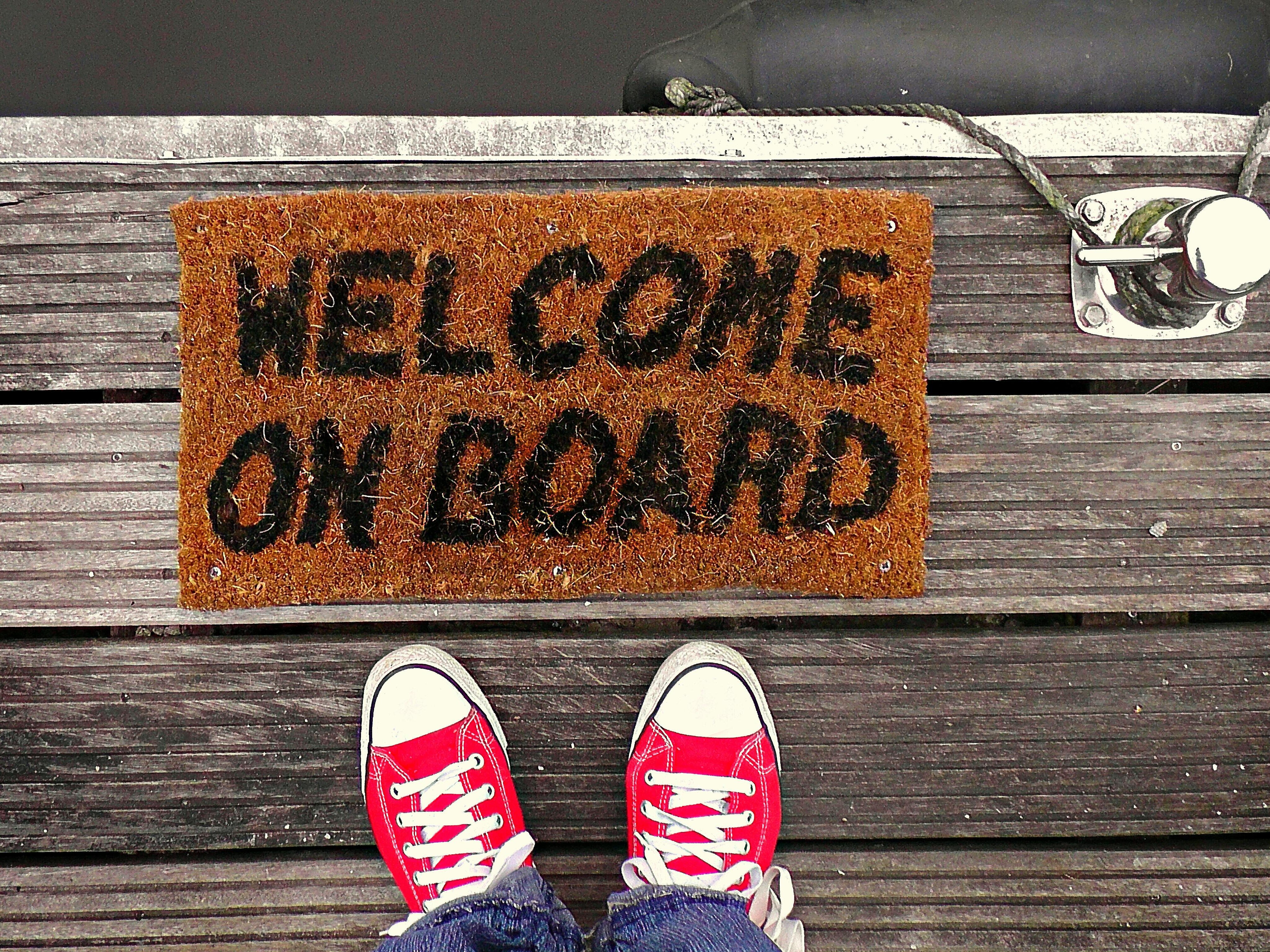 Person in roten Turnschuhen steht vor Fußmatte mit der Aufschrift "Welcome on board"