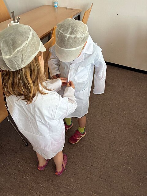 ein Kind hilft einem anderen beim Anziehen eines Kittels