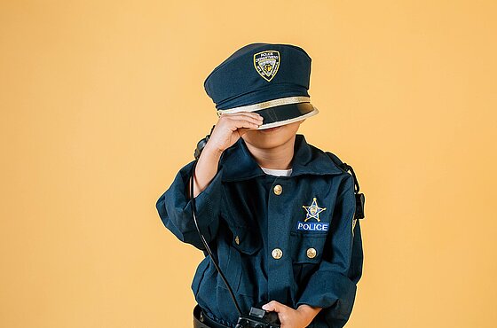 ein Kind in Polizeiuniform zieht die Mütze tief ins Gesicht