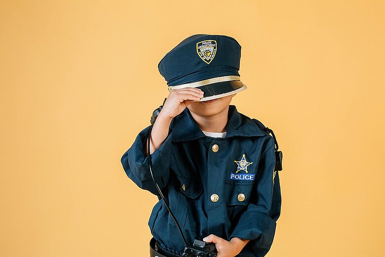 ein Kind in Polizeiuniform zieht die Mütze tief ins Gesicht