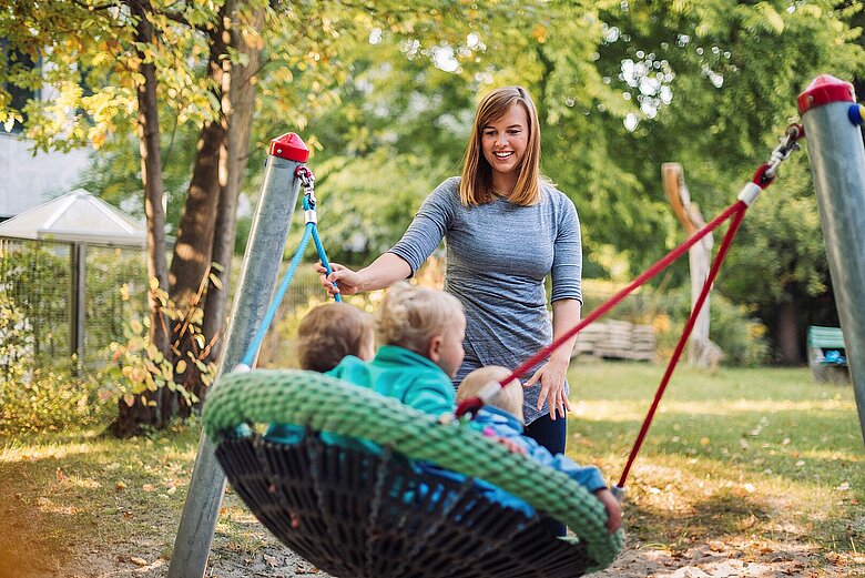 eine Erzieherin schaukelt Kinder in einer Nestschaukel