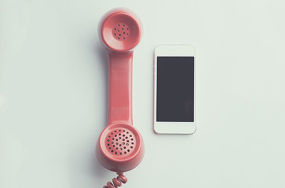 ein Smartphone neben einem altmodischen roten Telefonhörer