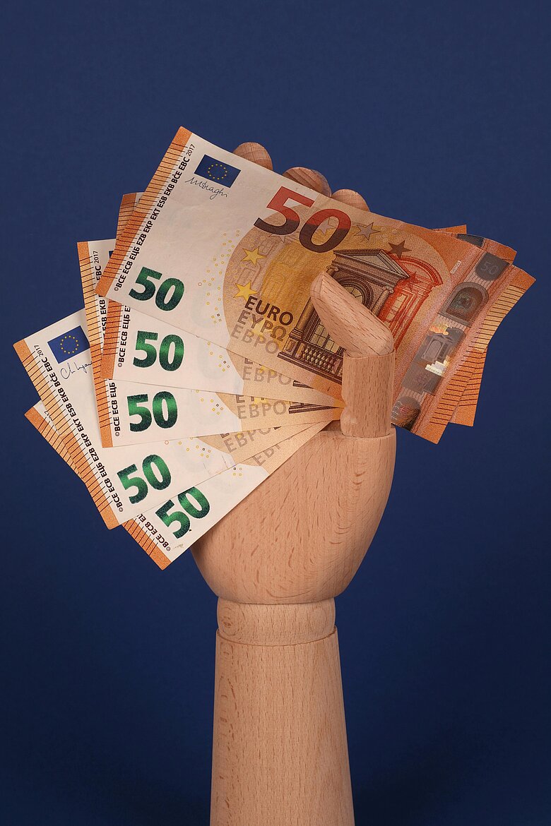 eine Holzhand hält Geldscheine