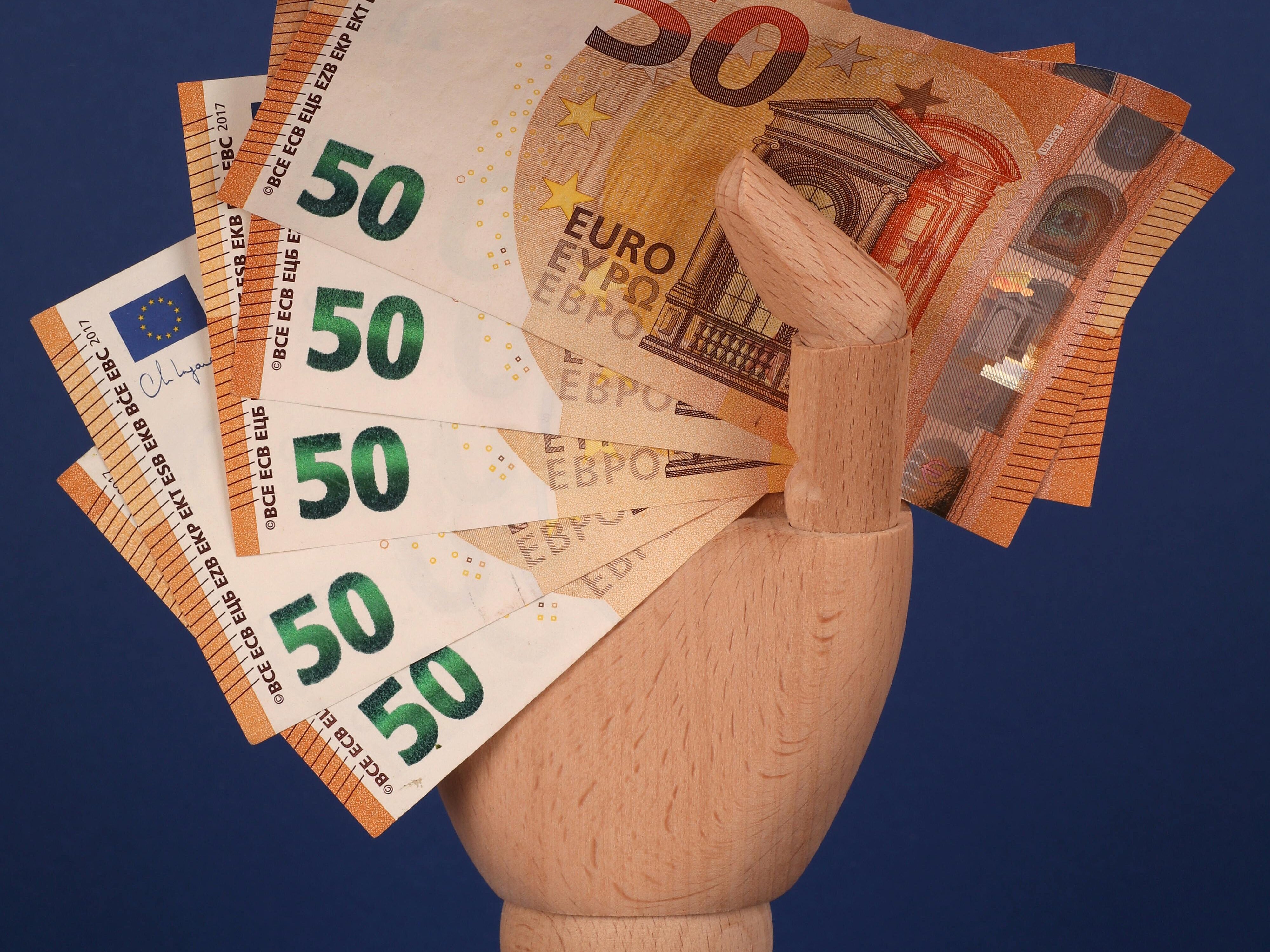 eine Holzhand hält Geldscheine