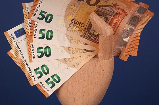 eine Holzhand hält Geldscheine