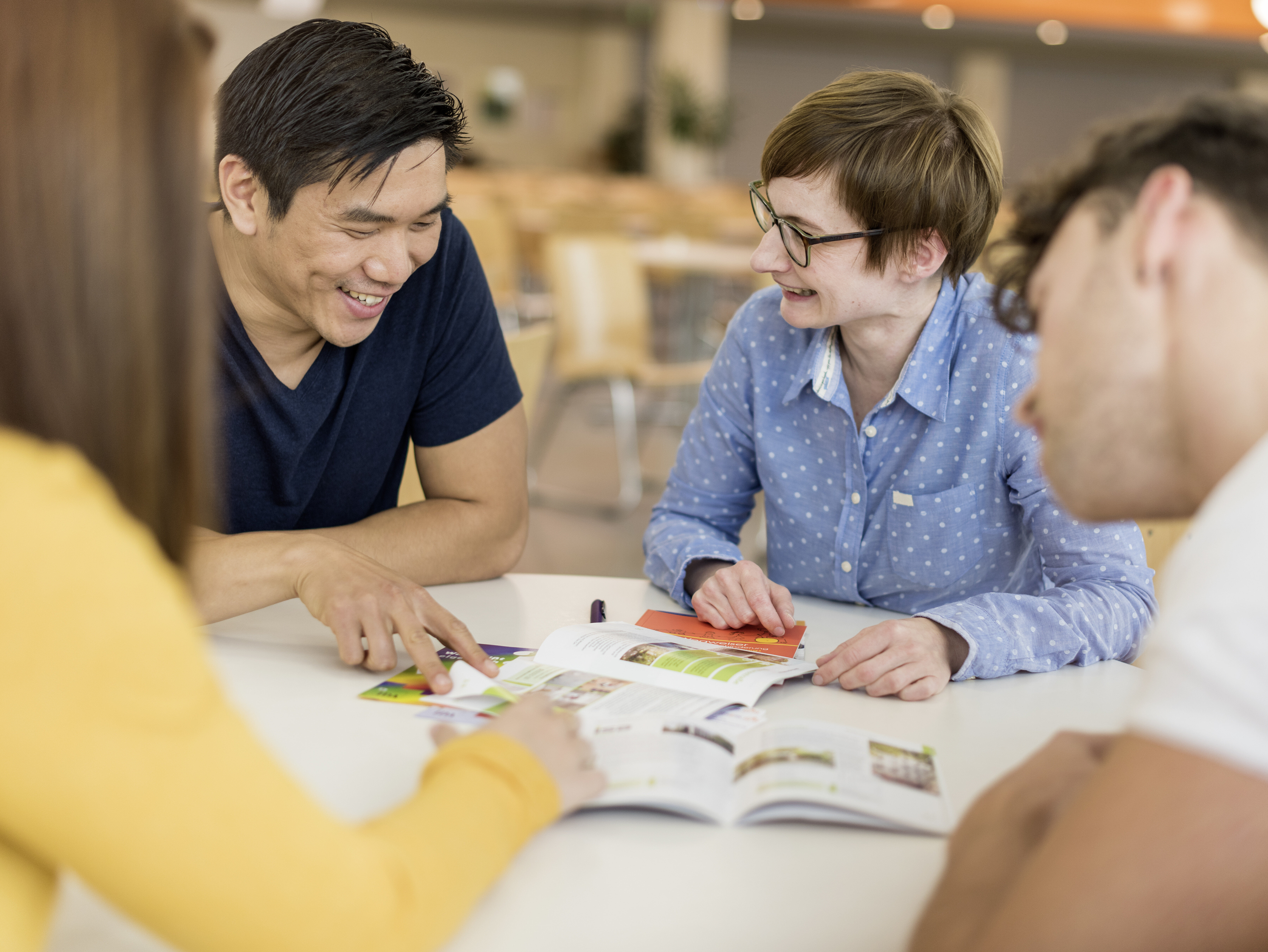 vier Personen an einem Tisch besprechen gut gelaunt Unterlagen auf dem Tisch