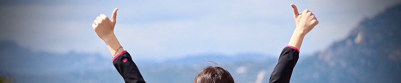 Rückansicht einer Frau in der Natur, die beide Daumen nach oben reckt