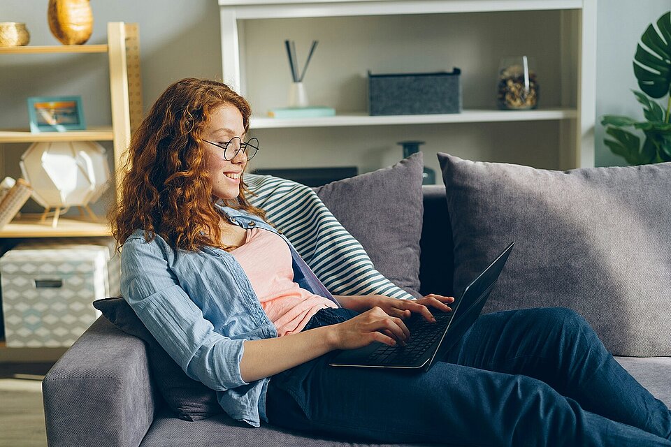 Frau auf Sofa arbeitet am Laptop