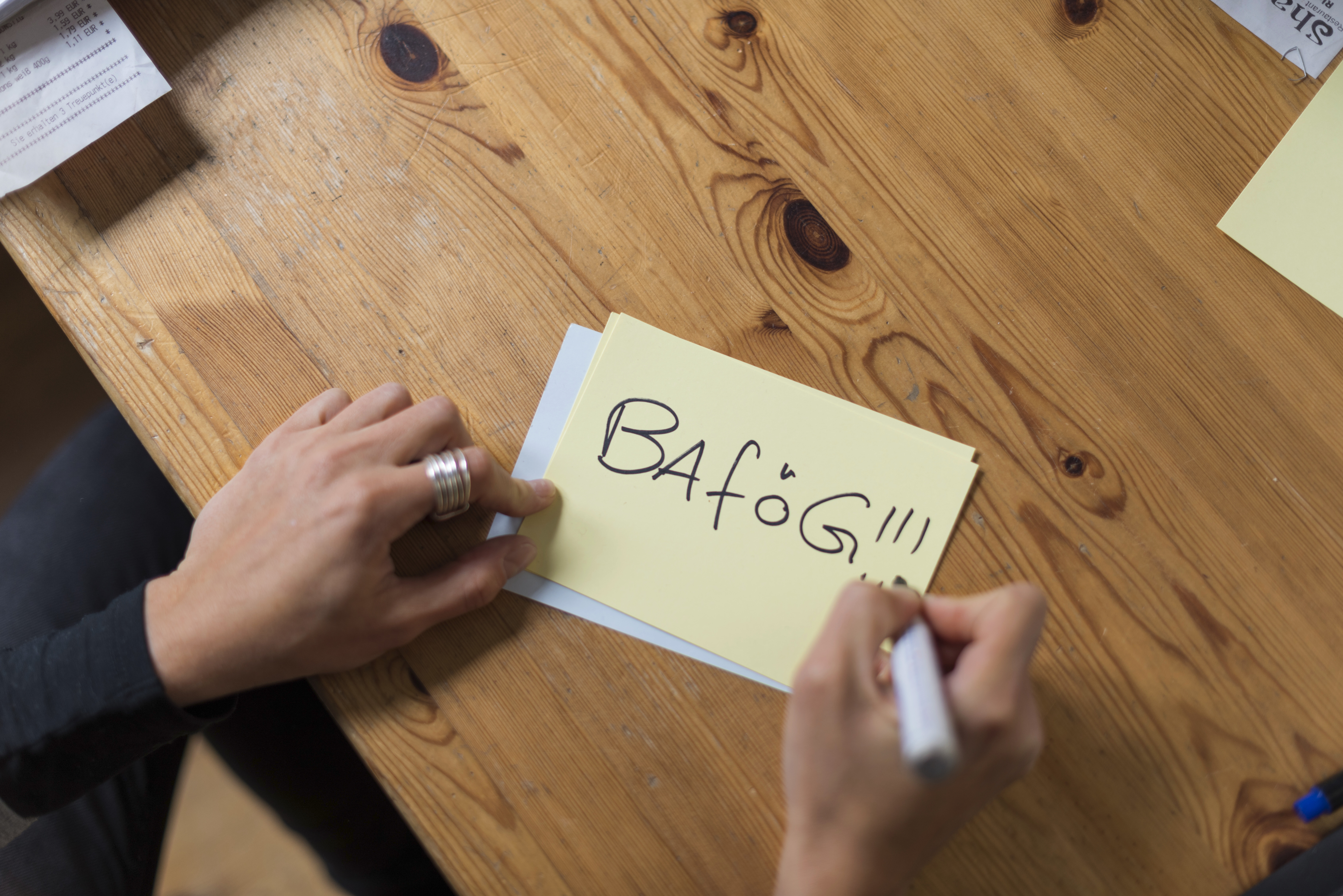Person schreibt "BAföG!" auf ein Post-it