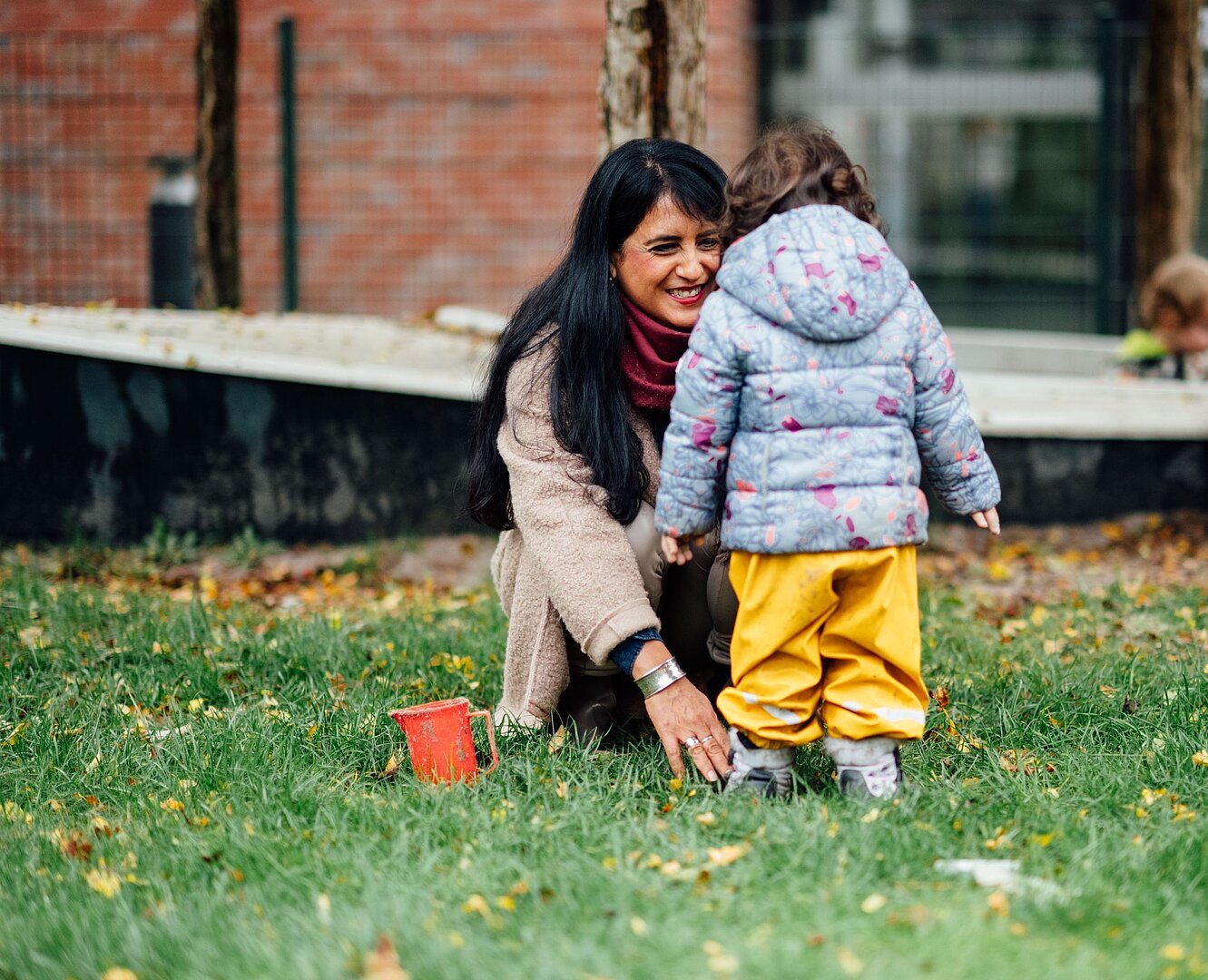 Fachkraft hilft einem Kind auf dem Außengelände einer Kita
